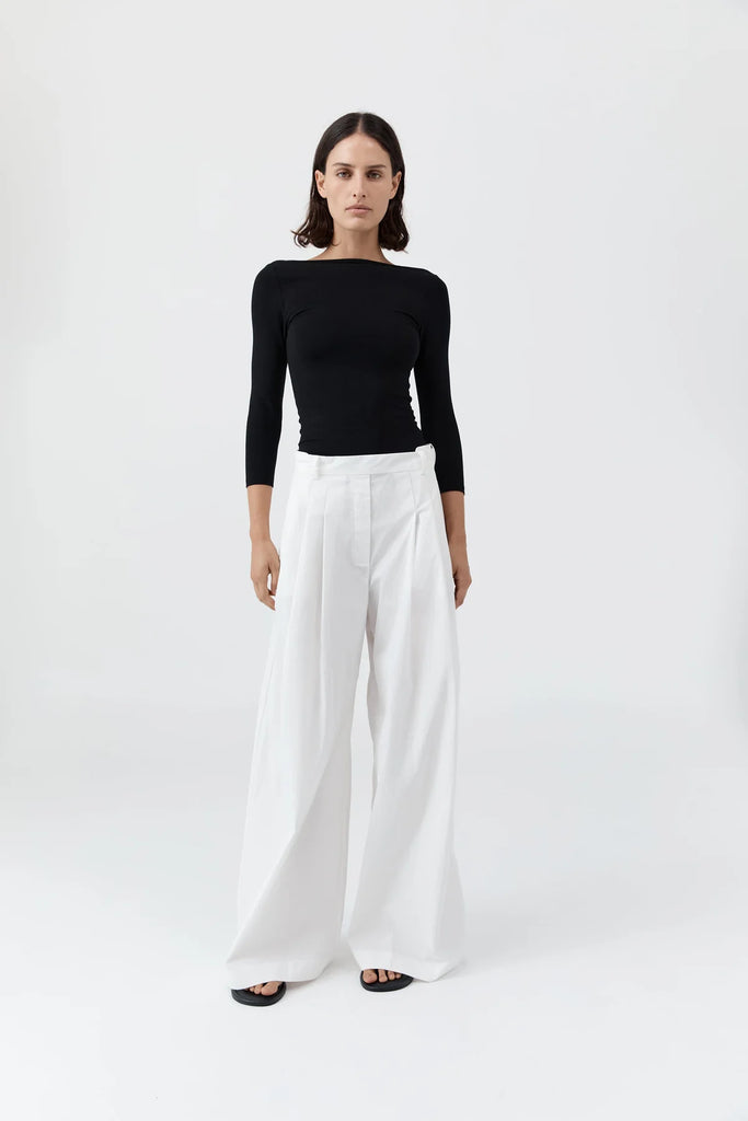 Woman wearing a black top and white pants on a white background