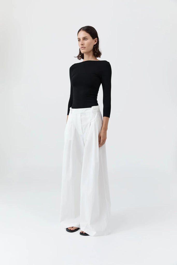 Woman wearing a black long-sleeve top and white wide-leg pants on a white background