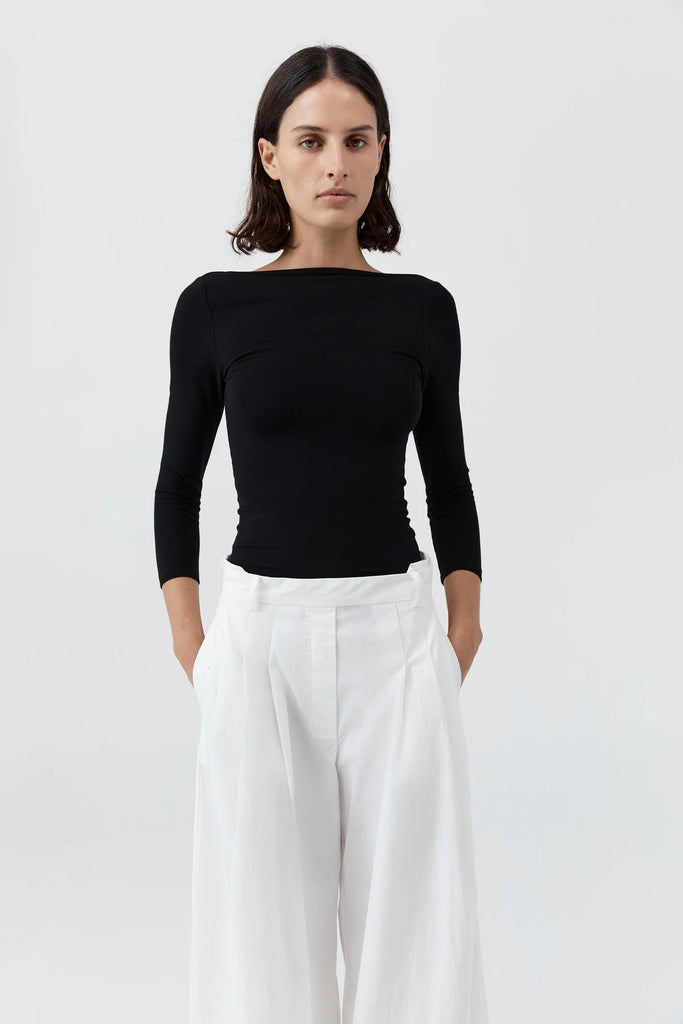 Woman wearing a black long-sleeve top and white pants on a white background