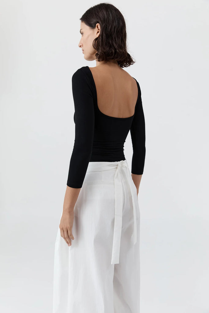 Woman wearing a black long-sleeve top and white pants on a white background