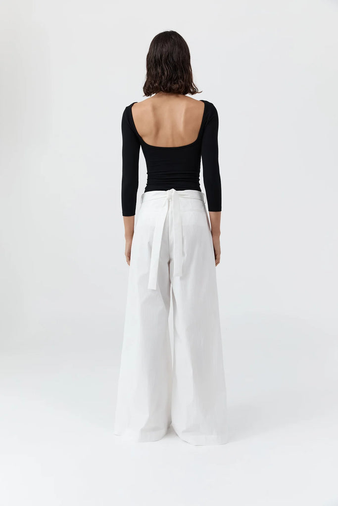 Person wearing a black open-back top and white wide-leg pants on a white background