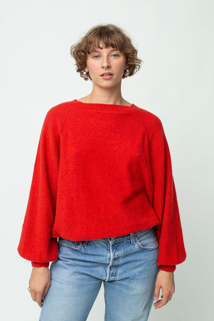 Person wearing a red sweater and light blue jeans on a white background