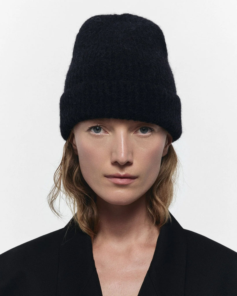 Person wearing a black knit beanie against a white background