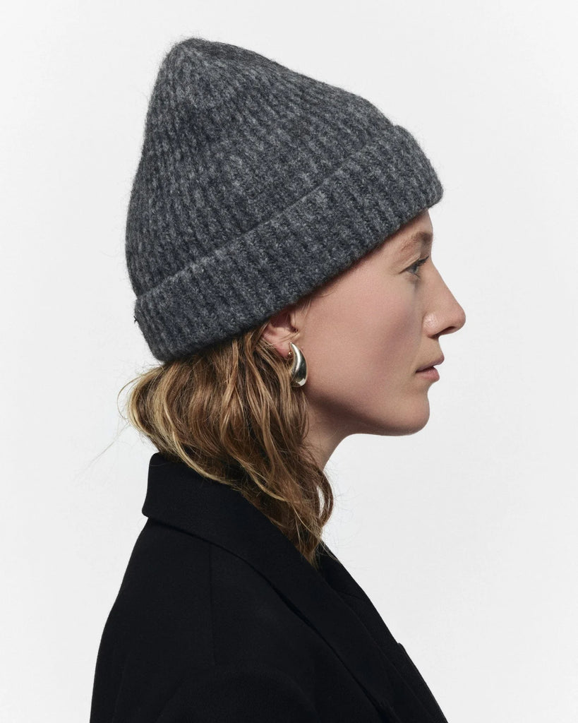 Person wearing a gray knit beanie and black coat on a white background