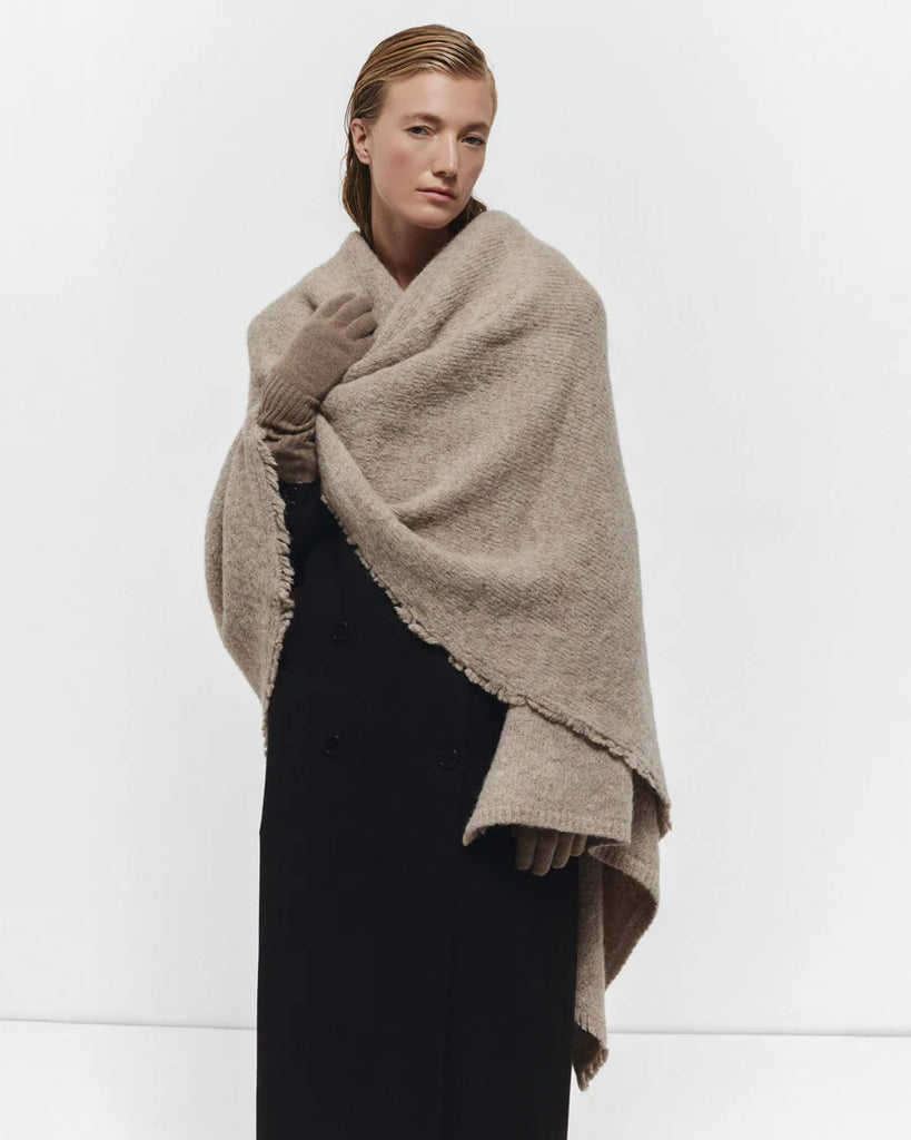 Woman wearing a beige shawl and gloves against a white background