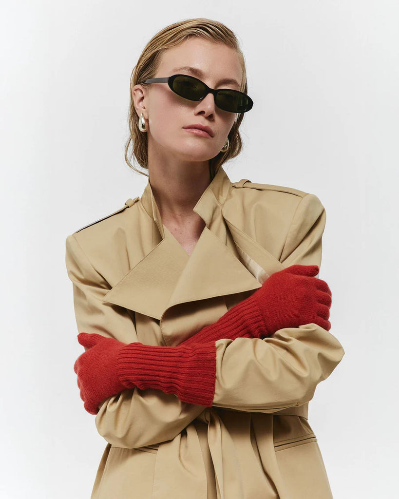 Person wearing a beige trench coat and red gloves with sunglasses on a white background
