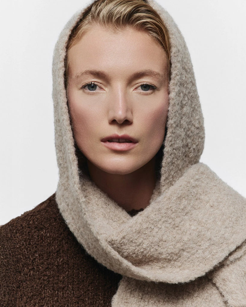 Person wearing a beige hooded garment against a white background