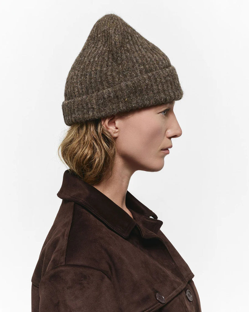 Person wearing a brown knitted beanie and coat on a white background