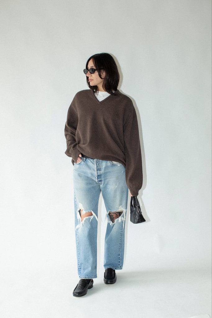 Person wearing a brown sweater and light blue jeans against a white background