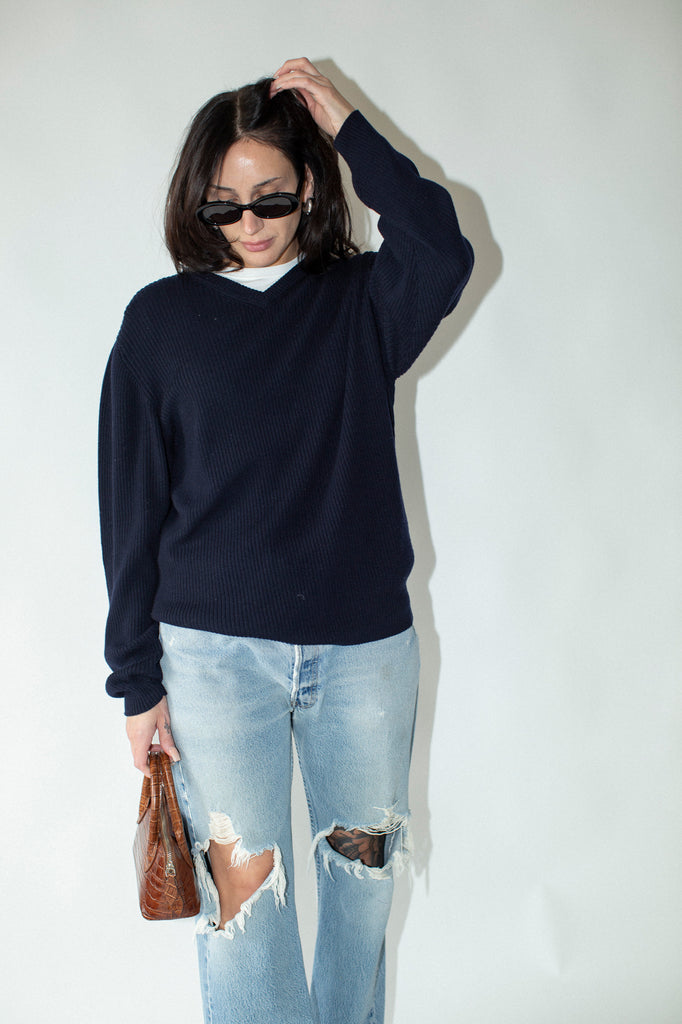 Person wearing a navy sweater and ripped jeans against a white background