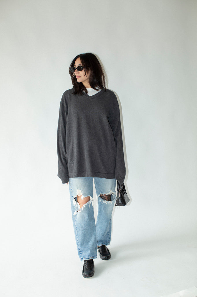 Person wearing a gray oversized sweater and ripped jeans on a white background