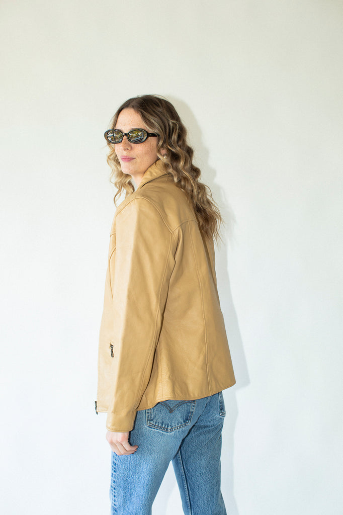 Woman wearing a tan jacket and sunglasses against a white background