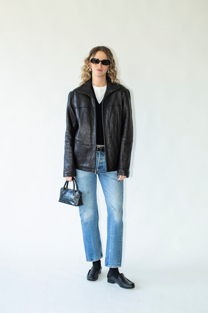 Person wearing a black leather jacket, white shirt, blue jeans, and black shoes on a white background