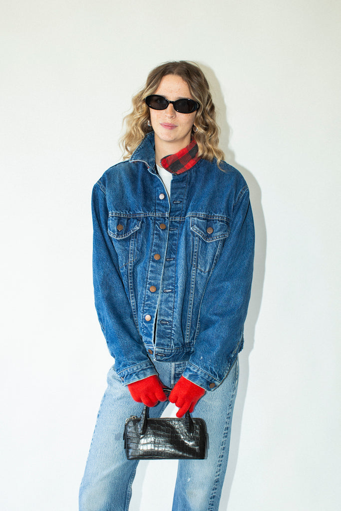 Person wearing a blue denim jacket, red gloves, and sunglasses against a white background