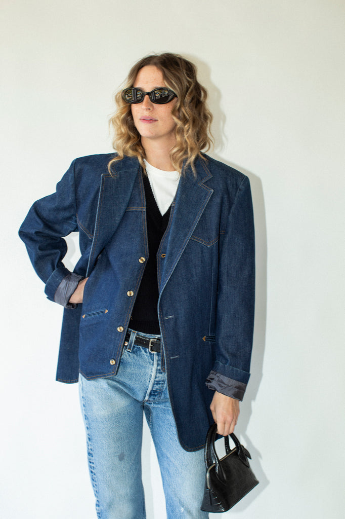 Woman wearing a blue denim jacket and jeans, holding a black handbag against a white background