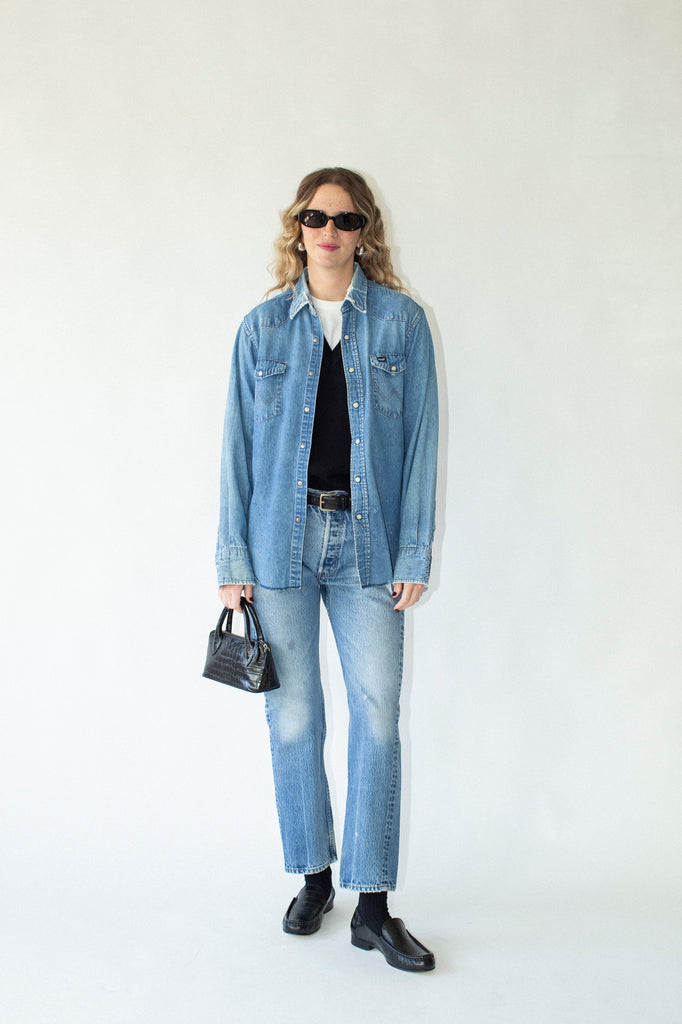 Person wearing a denim jacket, black shirt, and jeans on a white background