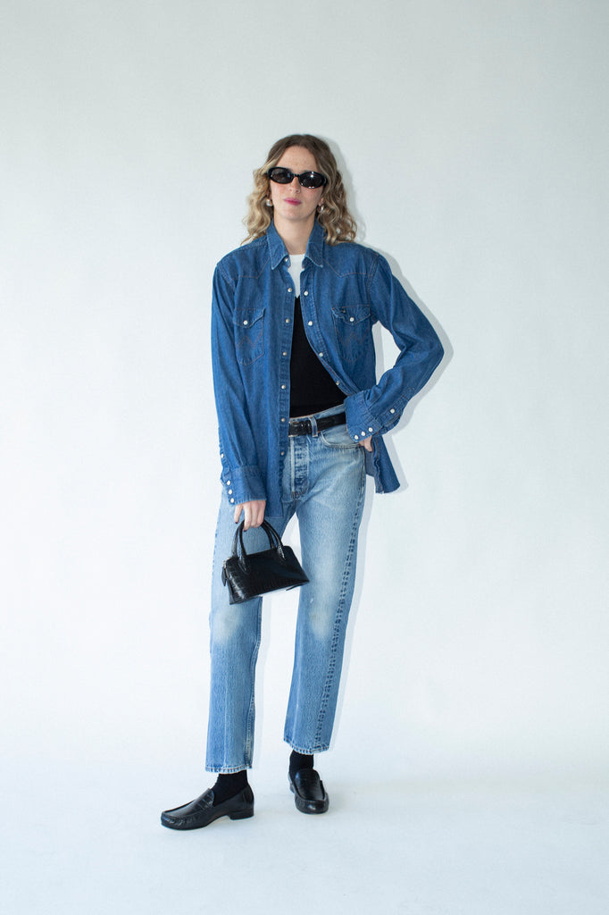 Person wearing a blue denim jacket, black shirt, and jeans on a white background