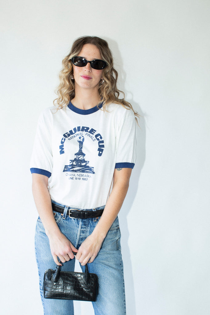 Woman wearing a vintage-style t-shirt with graphic design and sunglasses, standing against a plain background.