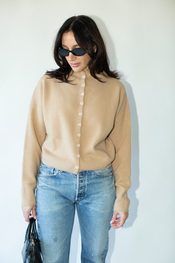 Woman wearing a beige cardigan and blue jeans against a white background