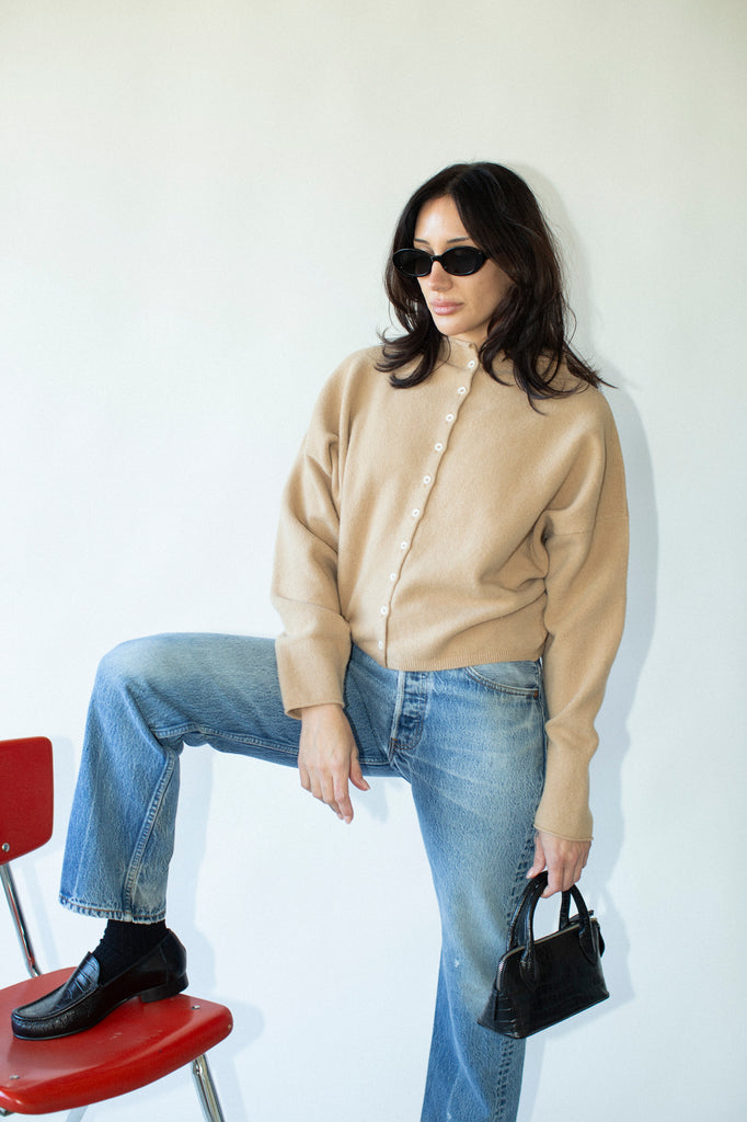 Woman in beige sweater and blue jeans sitting on a red chair against a white wall.