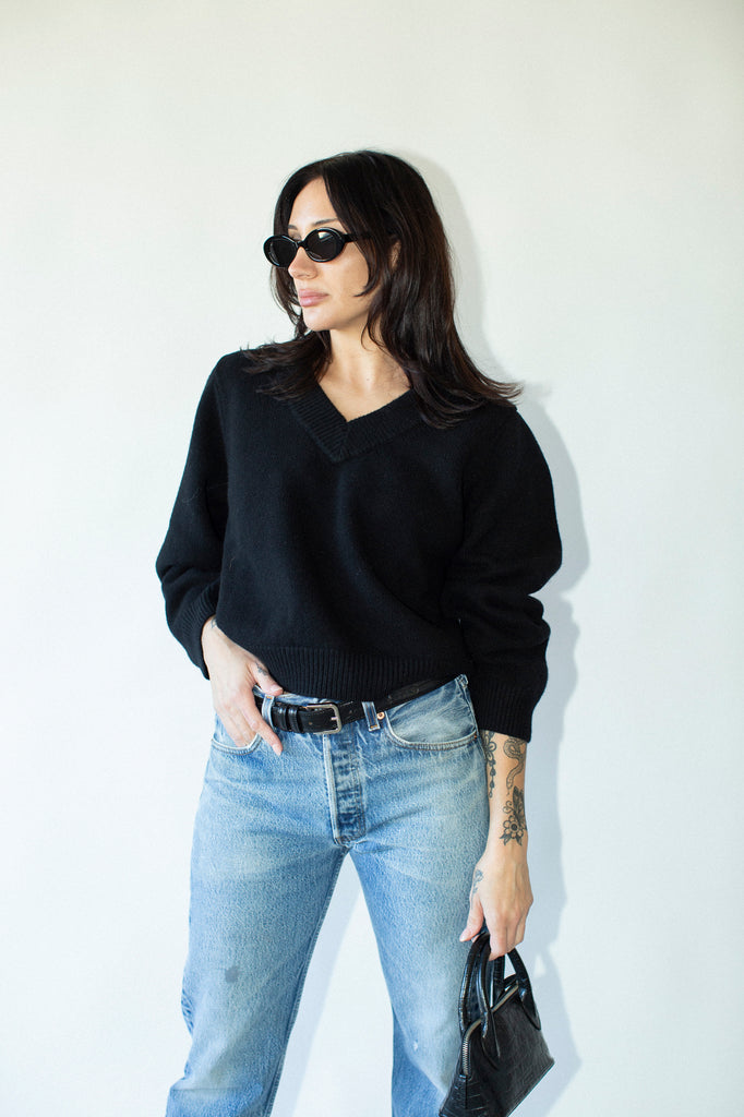 Woman wearing a black sweater and light blue jeans against a white background