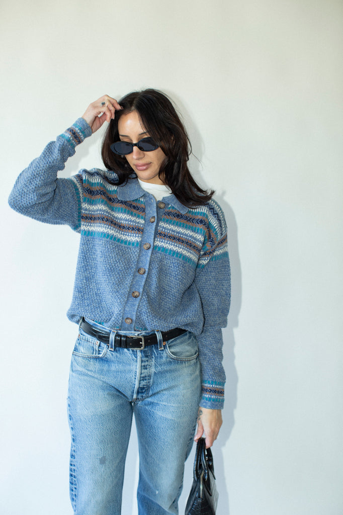 Woman wearing a blue patterned cardigan and jeans against a white background