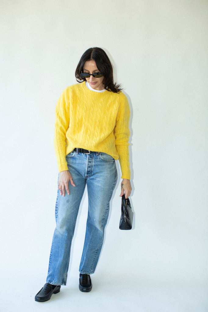 Person wearing a yellow sweater and blue jeans against a white background