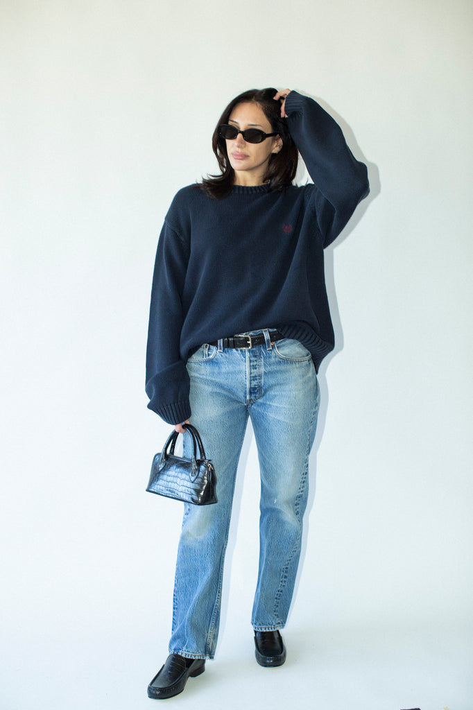 Person wearing a navy sweater, light blue jeans, and black shoes on a white background