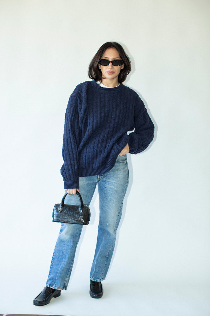Person wearing a navy sweater, light blue jeans, and black shoes against a white background