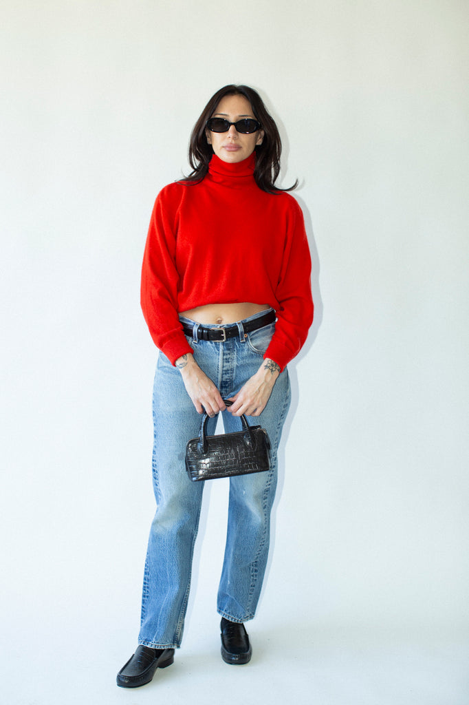 Person wearing a red sweater, blue jeans, and black shoes on a white background