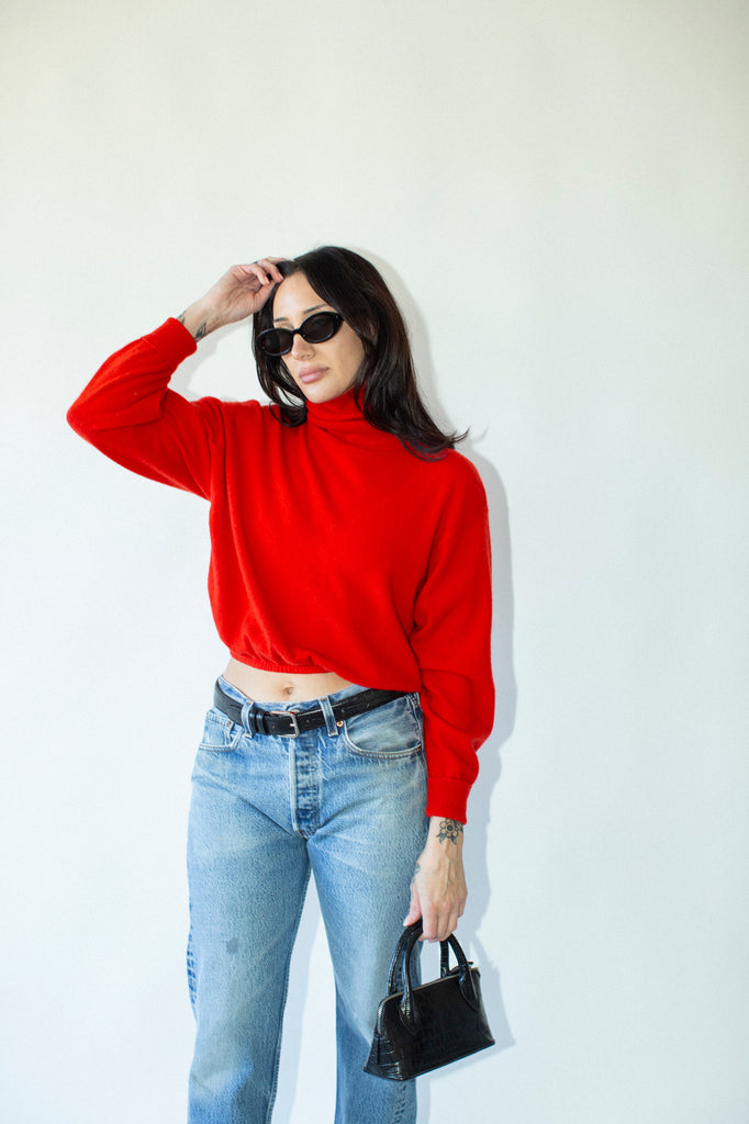 Woman wearing a red sweater and blue jeans against a white background