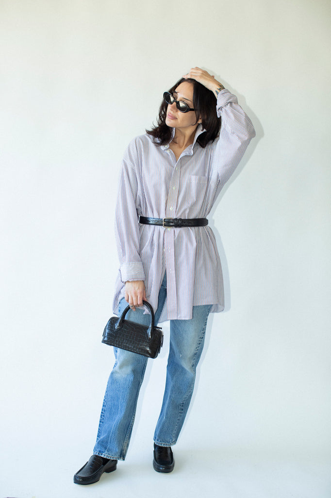 Woman wearing a light gray shirt, blue jeans, and black shoes against a white background