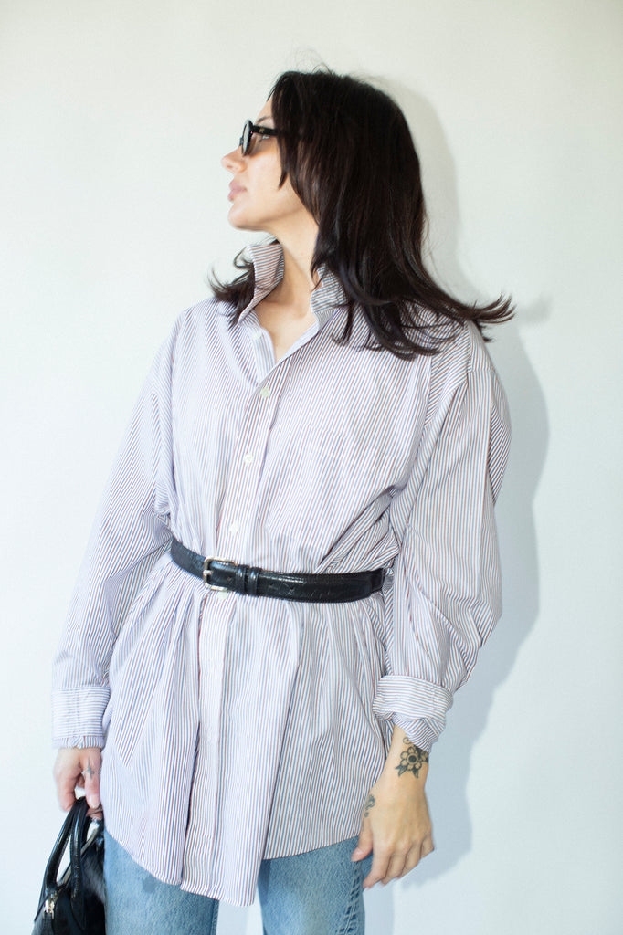 Woman wearing a light-colored shirt with a black belt against a white background