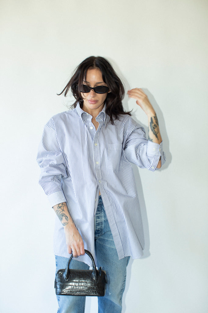 Woman wearing a striped shirt and jeans, holding a black handbag against a white background