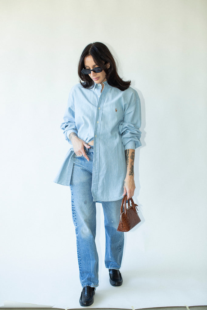Woman wearing a light blue shirt and jeans with sunglasses on a white background