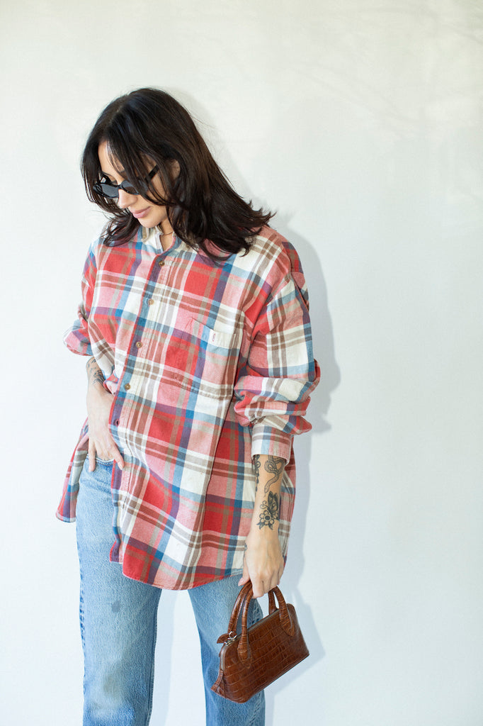 Person wearing a plaid shirt and jeans, holding a brown handbag against a white background