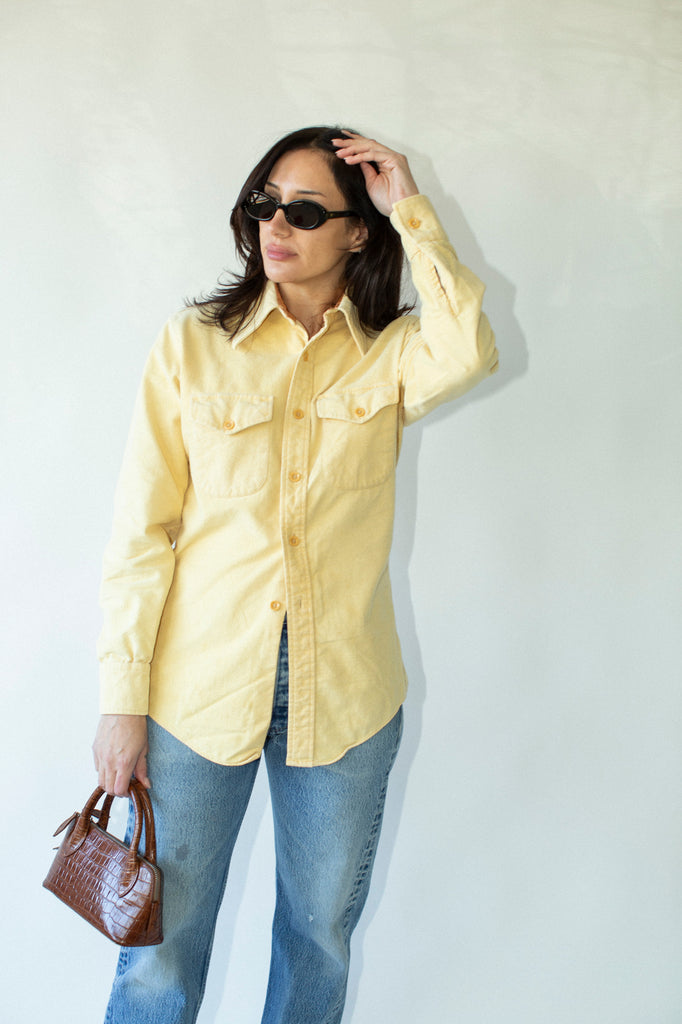 Woman wearing a yellow shirt and blue jeans against a white wall