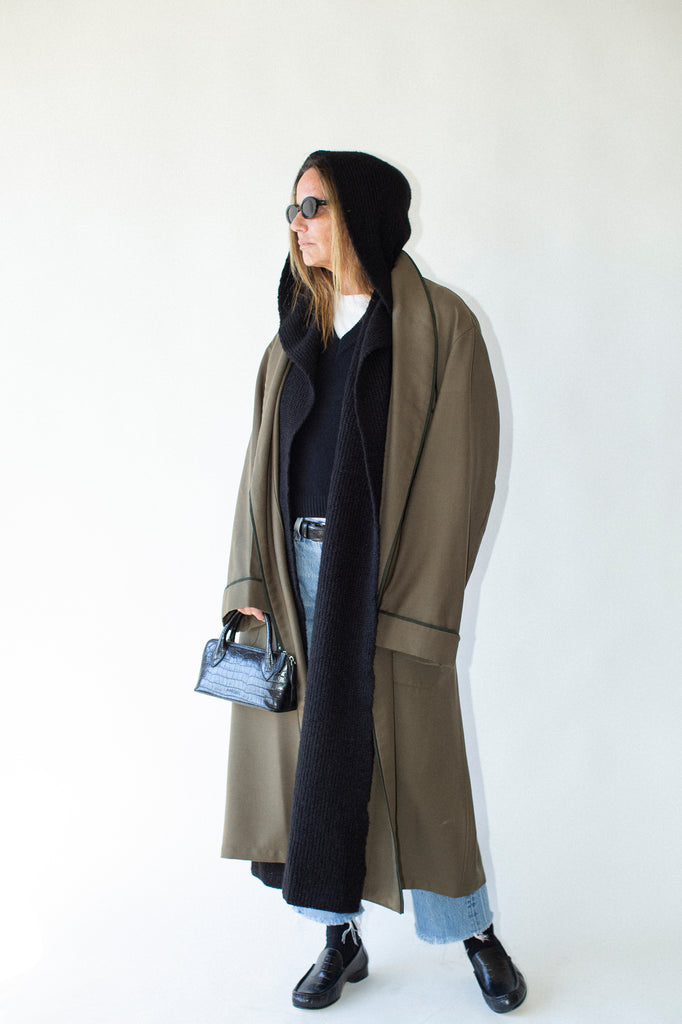 Person wearing a long coat and black hoodie against a white background