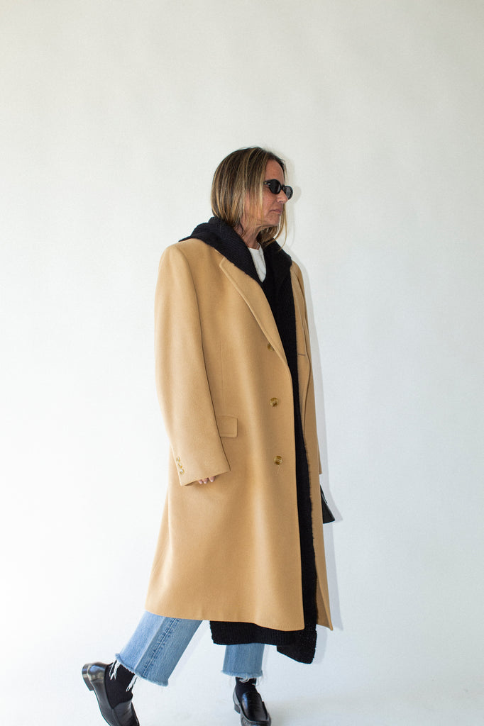 Person wearing a beige coat with a black hood against a white background