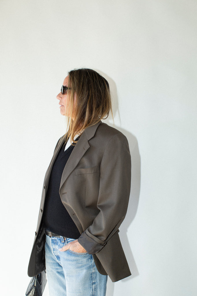 Person wearing a gray blazer and light blue jeans against a white background