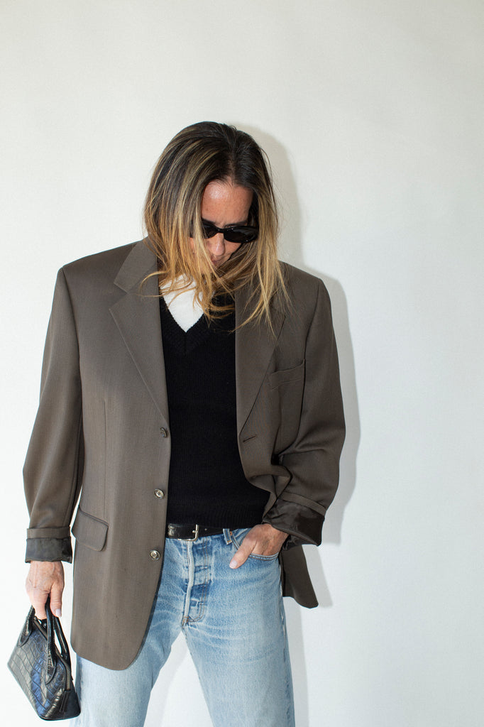 Person wearing a brown blazer, black shirt, and blue jeans against a white background