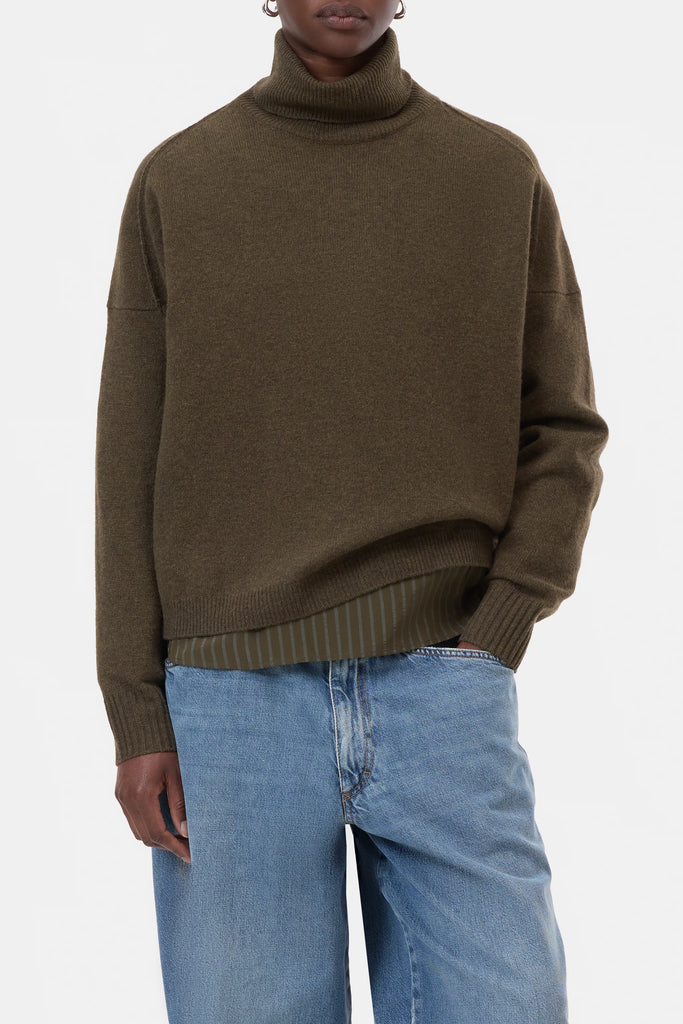 Person wearing a brown turtleneck sweater and blue jeans on a white background
