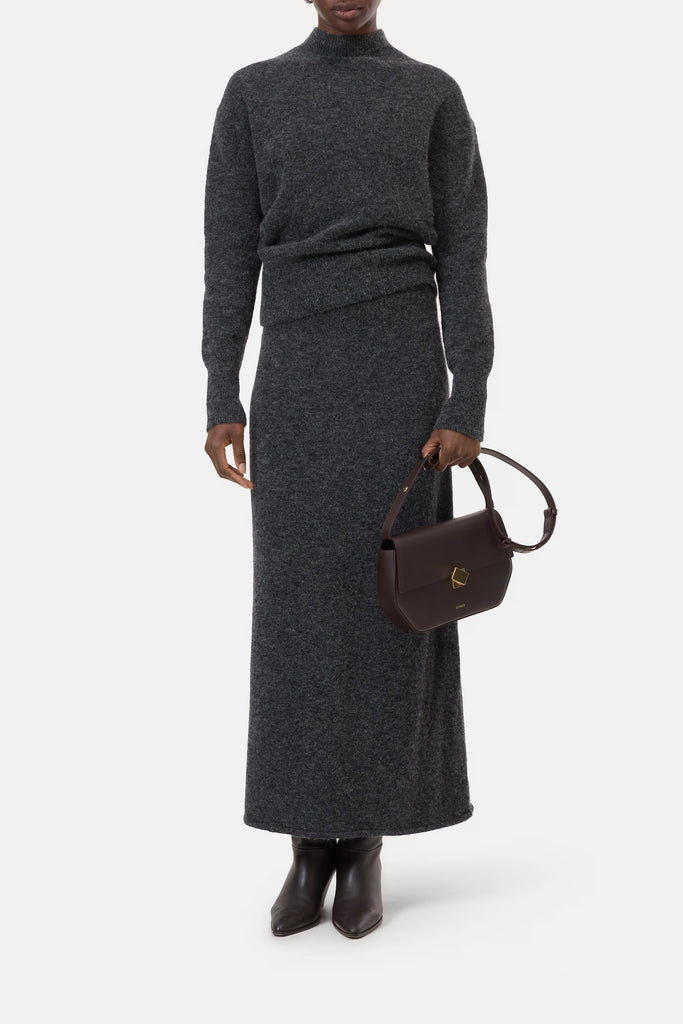 Person wearing a dark gray sweater and skirt set with a brown handbag on a white background