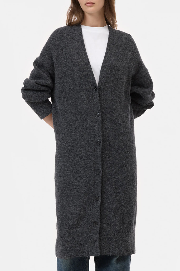 Person wearing a long gray cardigan over a white shirt on a light gray background