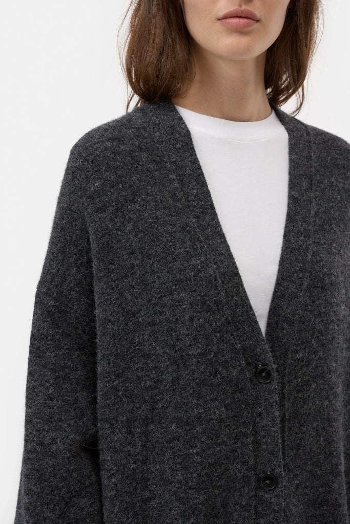 Person wearing a dark gray cardigan over a white shirt on a light gray background