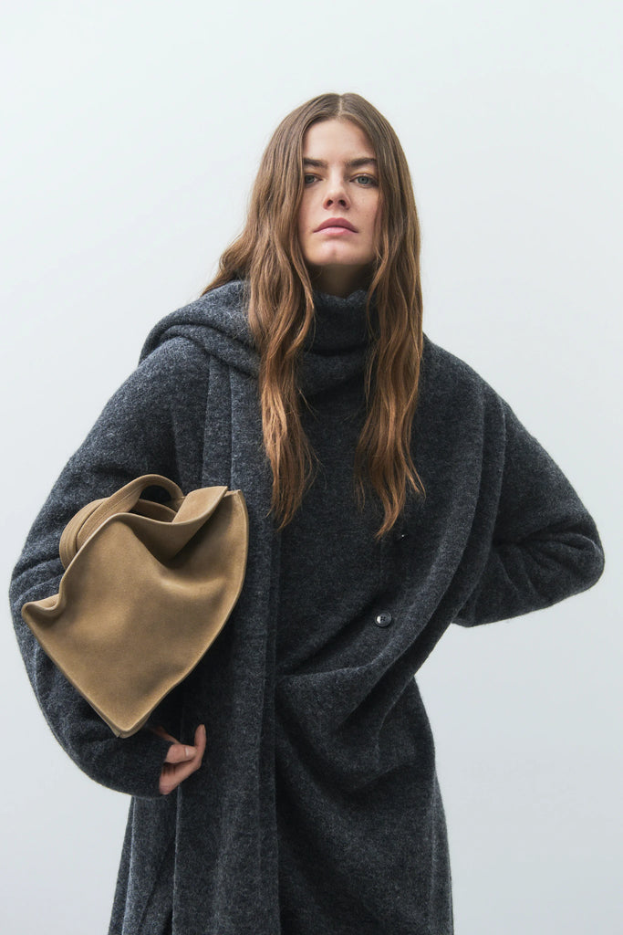 Woman wearing a dark gray coat holding a beige bag against a white background